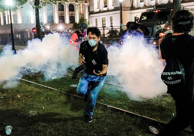 Un fotógrafo corre a ponerse a cubierto mientras la policía lanza gas lacrimógeno durante la tercera noche de disturbios en Kenosha, Wisconsin.