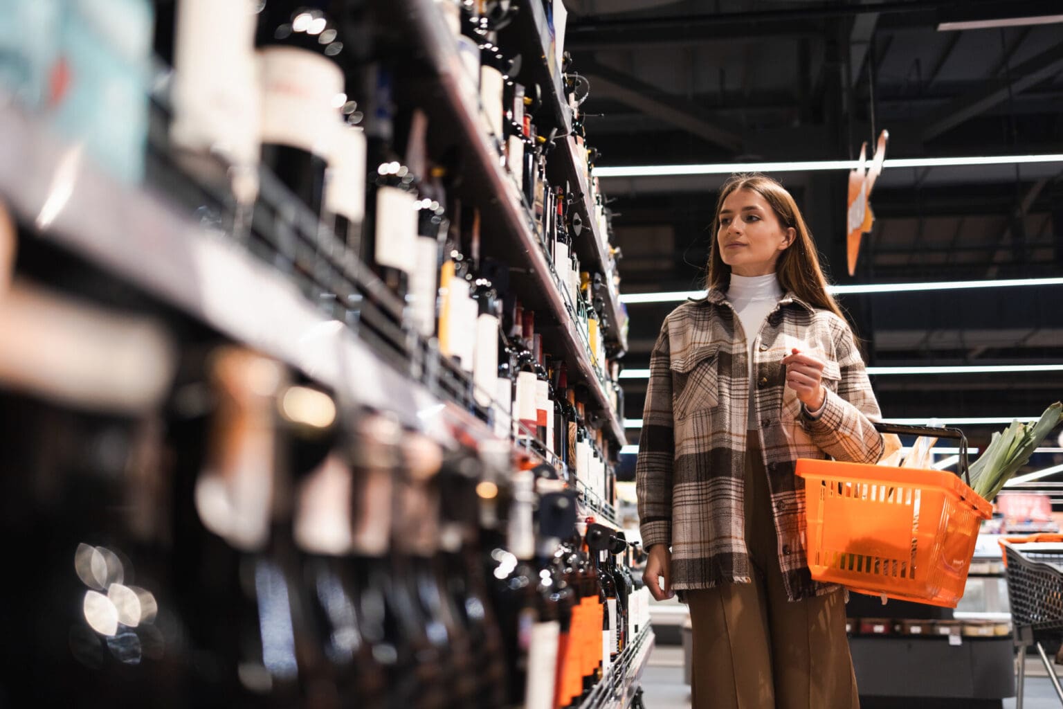 young woman with basket looking wine while shoppin 2023 11 27 05 35 28 utc scaled 1