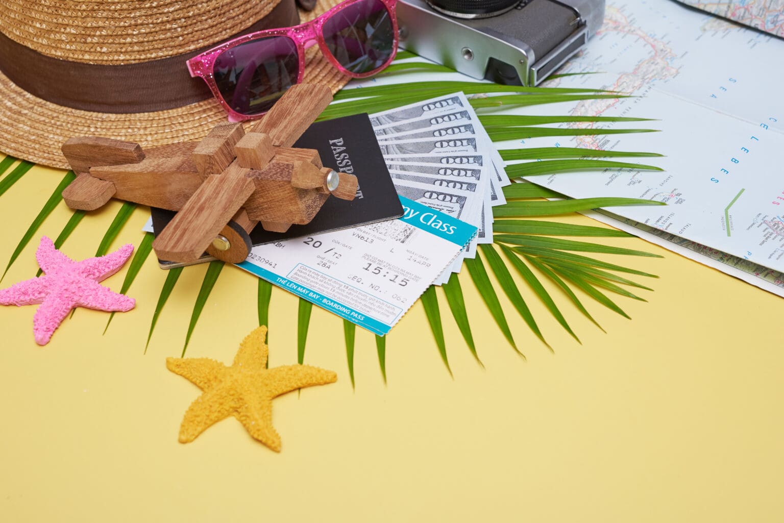 flat lay traveler accessories yellow surface with palm leaf camera shoe hat passports money air tickets airplanes sunglasses top view travel vacation concept