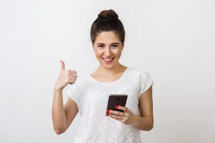 stylish young woman with attractive face holding smartphone showing thumb up positive gesture smiling good mood using mobile device isolated